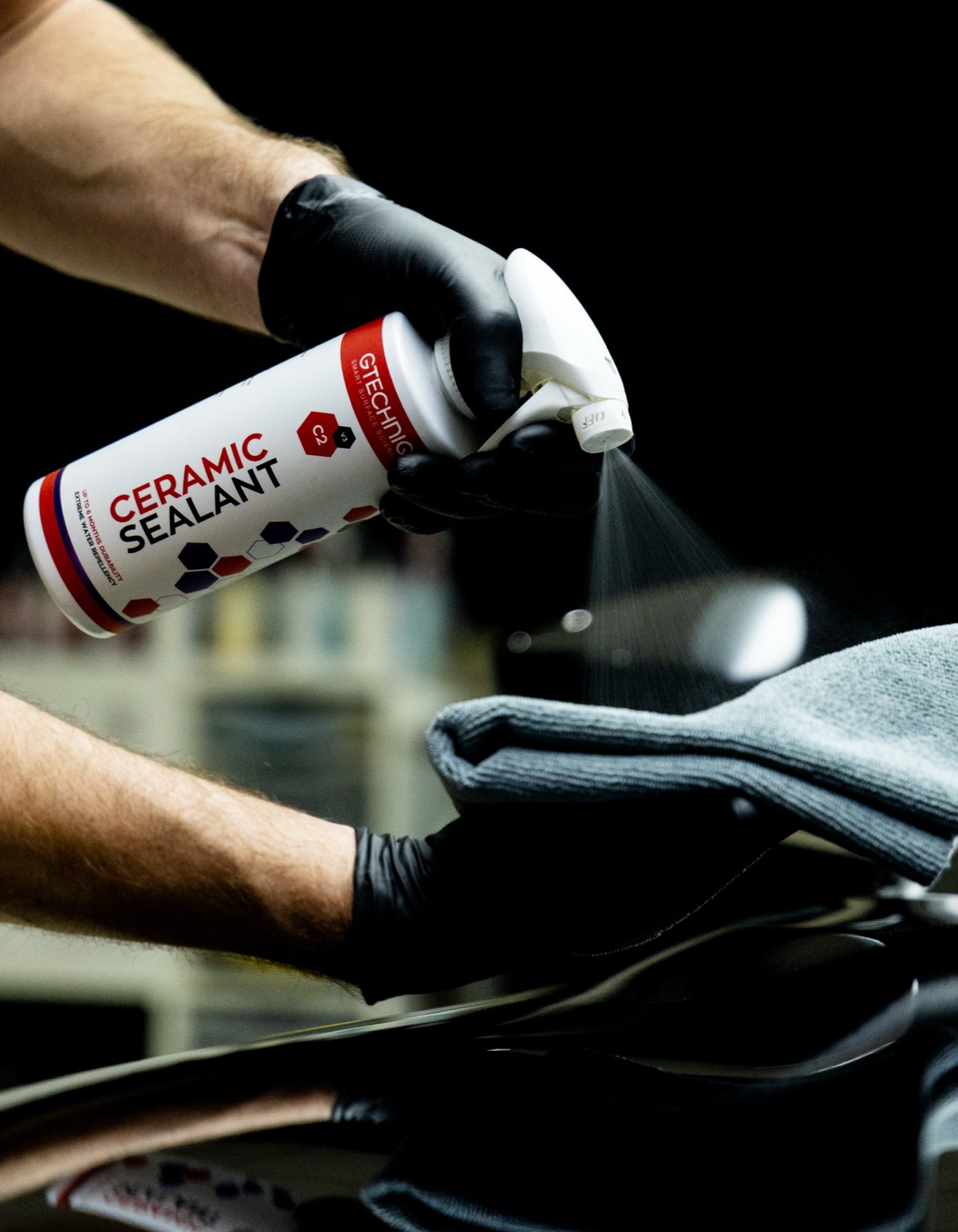 Gtechniq C2 Ceramic Sealant being sprayed onto a microfibre over the dark paintwork of an Aston Martin DBS